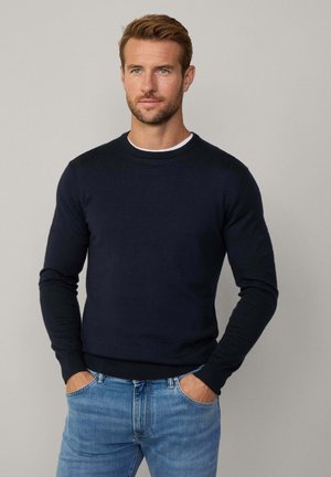 Maglione girocollo blu scuro in materiale morbido, design aderente, maniche lunghe, polsini e orlo a coste, abbinato a jeans blu chiaro.