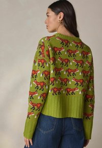 Green knitted sweater featuring a pattern of orange foxes, ribbed hem, and long sleeves. Fabric has a soft texture and medium thickness.