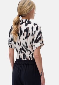 Koszulka z krótkim rękawem i kołnierzykiem, wykonana z lekkiego materiału. Posiada abstrakcyjny wzór w kolorze czarnym i kremowym z jasnoróżowymi akcentami. Elastyczny pas na dole.