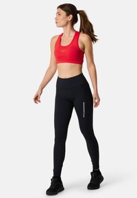 Red sports bra with a round neckline, paired with high-waisted black leggings featuring a zippered pocket and reflective accent.