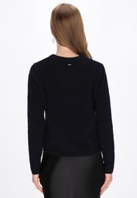 Marineblauwe trui met lange mouwen, ronde hals en ribgebreide manchetten. Zachte textuur; heeft een klein logo tag op de bovenrug.