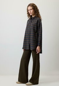 Srajca na gumbke z zeleno-rjavimi črtami, kombinirana z olivno širokimi hlačami. Srajca ima klasičen ovratnik in sproščen kroj.