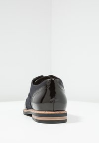 Herren-Schuh mit einem schwarzen Lackleder-Absatz, Obermaterial aus marineblauem Wildleder, runder Zehenform und einer leicht braunen Korkakzent-Sohle.