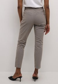 Hellgraue, taillierte Hose mit glatter Textur, dekorativen Gesäßtaschen und einem schmalen Knöchellänge. Getragen mit schwarzen, hohen Mules.