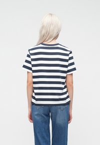 Medvilninis marškinėliai su tamsiai mėlynomis ir baltomis horizontaliomis juostomis, trumpomis rankovėmis, apvalia iškirpte ir laisvu siluetu, derinami su mėlynos džinsinės medžiagos kelnėmis.