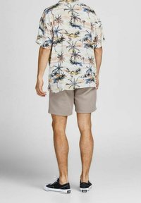 Camicia a maniche corte, stampata con palme e fenicotteri in colori pastello, abbinata a pantaloni corti beige e sneakers nere.