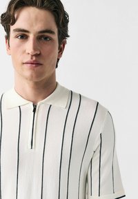 White short-sleeve polo shirt with navy vertical stripes, a zippered collar, and a soft texture. Simple, clean design without embellishments.
