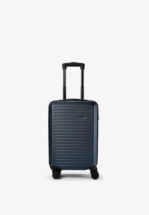 Valise rigide bleu foncé avec des rainures horizontales, poignée rétractable et quatre roues pivotantes, debout sur fond blanc.