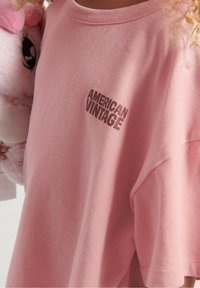 Lyserød bomulds t-shirt med relaxed fit, der har et trykt "AMERICAN VINTAGE" logo i mørkebrun på brystområdet.