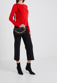 Rode gebreide trui, zwarte cropped broek en zwarte enkellaarsjes met een puntige neus. Zwarte gewatteerde handtas met gouden kettinghengsel.
