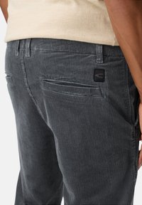 Grijze corduroy broek met verticale ribbelstructuur, met achterzakken en een zwart logo-patch op de tailleband.