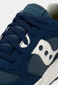 Tamsiai mėlyni sportiniai bateliai, pagaminti iš tekstūruotos zomšos, tinklelio audinio ir baltos logotipo detalės. Storos tamsiai mėlynos spalvos raišteliai ir paminkštinta liežuvėlis su prekės ženklu.