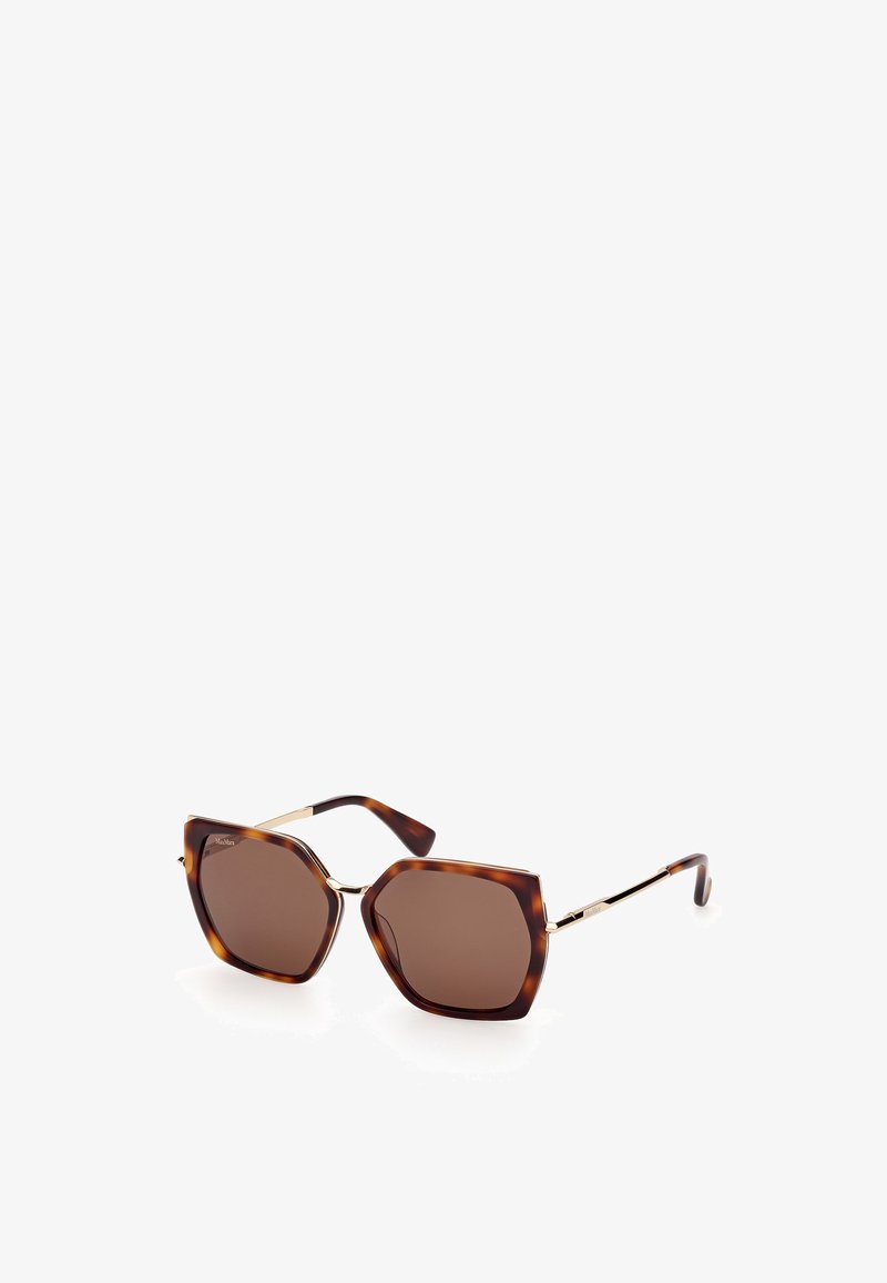 Gafas de sol de carey con una montura hexagonal, lentes marrón oscuro, acentos dorados en las patas y textura de plástico suave.