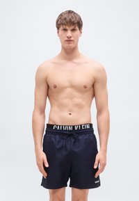 Μαύρα μπλε μαγιό σορτς με μαύρη ελαστική ζώνη μέσης που φέρει λευκό λογότυπο. Τα σορτς έχουν λεία υφή και άνετη εφαρμογή.