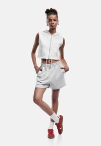 Grauer kurzer Zip-Hoodie mit Fronttaschen, kombiniert mit passenden grauen Shorts. Das Modell trägt rote Sneaker und weiße Socken, was einen lässigen Look zeigt.