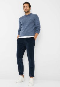 Blå strikket sweater med rund hals, parret med marineblå fløjlbuede bukser og hvide sneakers. Har ribbede manchetter og en afslappet pasform.