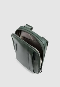Bolso mensajero de cuero verde con cierre de cremallera, que presenta un exterior suave y texturizado y una forma rectangular simple. El interior está forrado con tela.