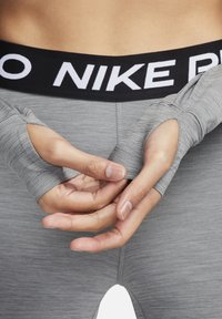 Top de manga larga gris con agujeros para los pulgares, superpuesto a una cinturilla gris a juego que presenta "NIKE PRO" en letras blancas en negrita. Textura suave.