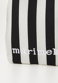 Black and white striped bag with ribbed texture. Embroidered "marimekko" logo in white. Material appears durable and stretchy.