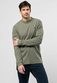 Groen langemouwen crewneck shirt met een gestructureerd patroon, voorzien van geribde boorden en een klein logo op de linkerkant van de borst. Gecombineerd met donkere jeans.