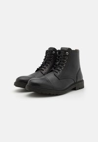 Botas de tobillo de cuero negro con superficie texturizada, punta redonda y sistema de cordones. Presentan ojales de metal y una suela de goma duradera.