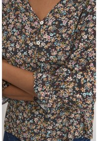 Blus med blommönster mot mörk bakgrund, flerfärgade blommor, tre knappar och volangkantade ärmslut. Lätt och mjukt tyg.