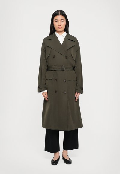 Olive green trench coat with double-breasted buttons, wide collar, belted waist, and front pockets; paired with black wide-leg pants and flats.