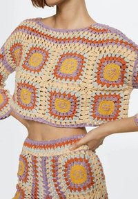 Ensemble en crochet composé d'un crop top oversize et d'une jupe mi-haute, de couleur beige, orange, violet et bleu, avec des motifs floraux carrés.