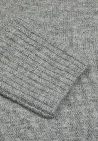 Pilkas megztinis su vartomomis rankogaliais, pasižymintis minkšta, tekstūrine medžiaga ir subtiliu įvairių pilkumo atspalvių raštu.