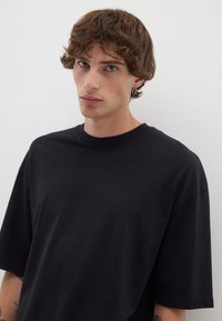 T-shirt nera oversize realizzata in un tessuto morbido e levigato. Collo a giro, maniche corte, senza motivi o decorazioni visibili. Design semplice.