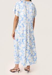 Lång, blå blommig klänning med korta ärmar, vit blommig tryck, lös passform, samlad midja, mjukt tyg, ankel-längd, i kombination med svarta sandaletter med remmar.