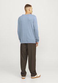 Lichtblauw langemouwen shirt met een relaxte pasvorm, geribbelde textuur en ronde halslijn, gecombineerd met donkerbruine broek en witte sneakers.