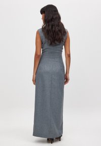 Ilga, prigludusi suknelė iš pilkos tekstūruotos medžiagos, be rankovių, tiesaus silueto, siekianti kulkšnis, su minimaliais akcentais.