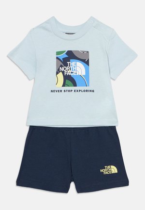 Lyseblå kortermet t-skjorte med fargerikt North Face-logo og teksten "Never Stop Exploring", kombinert med marineblå shorts med gul logo.
