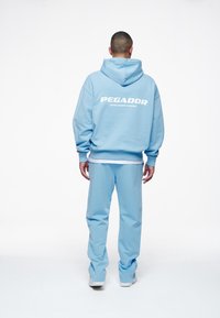 Sudadera con capucha azul claro y pantalones deportivos a juego. La sudadera tiene el logo "PEGADOR" en la espalda. Tejido suave y ajuste relajado.