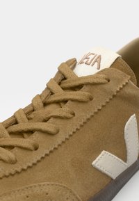 Καφέ σουέτ αθλητικά παπούτσια με επίπεδους κορδόνια, λευκή λογότυπο διακόσμηση και ραμμένα σχέδια. Διαθέτουν υφασμάτινη σόλα με υφή και ετικέτα γλώσσας σε αντίθεση.