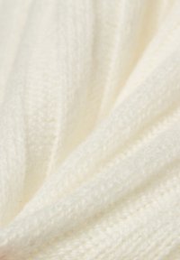 Weißer Strickstoff mit einer weichen Textur, der ein geripptes Muster aufweist, das unterschiedliche Tiefen und einen sanften Glanz erzeugt.