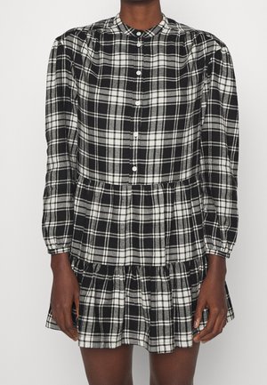 Schwarz-weiß kariertes Kleid mit rundem Kragen, langen Ärmeln, Knopfverschluss und gestuften Rüschensaum. Hergestellt aus leichtem Stoff.