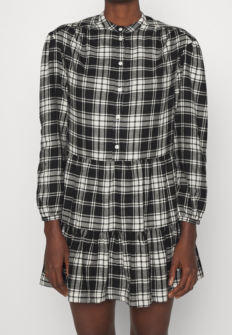 Svart- och vitrutigt klänning med rund krage, långa ärmar, knappstängning och lager-på-lager volangkant. Tillverkad av lätt material.