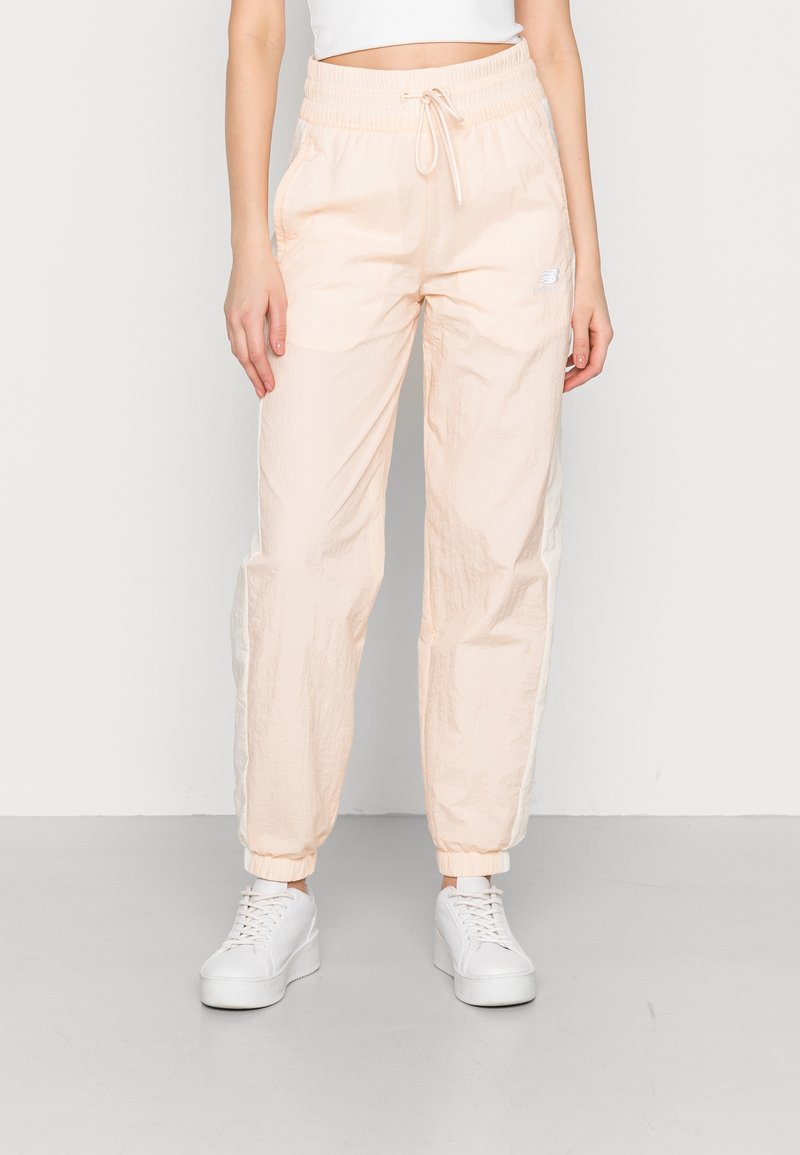 Světle broskvové tepláky s elastickým pasem, nastavitelnou šňůrkou, dvěma bočními kapsami a elastickými manžetami. Na boku jsou decentní logo.