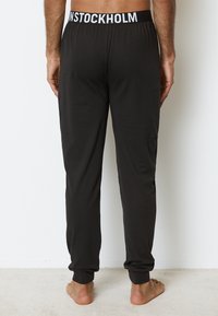 Svarta loungebyxor med elastisk midja som visar "STOCKHOLM" i vitt. Slät tyg, avsmalnande ben och ankelmuddar för en åtsittande look.