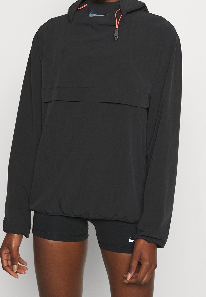 Personne portant une veste de sport noire à capuche avec cordons et un short ajusté noir avec un logo Nike blanc sur la jambe gauche.