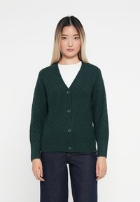 Cardigan en tricot vert avec un motif en diamant, doté d'un col en V, de poignets côtelés et de cinq boutons verts sur le devant.