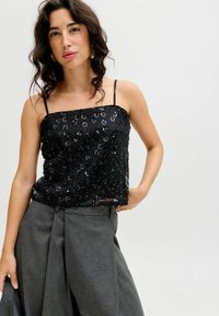 Melnas seklaņu topiņš ar plānām siksnām, ar kvadrātu izgriezumu un brīvu piegriezumu, apvienots ar pelēkām krokotām biksēm.