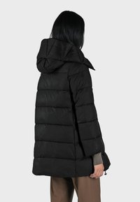 Giacca a vento nera con cappuccio, caratterizzata da un design trapuntato, materiale strutturato e lunghezza media. Include una coulisse all'orlo.