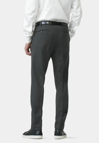 Pantalons gris ajustés avec une coupe slim, présentant une texture lisse, deux poches arrière et un motif à carreaux discret. Associés à des baskets noires.
