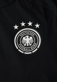 Mustapohjainen urheilu pelipaita, jossa on pyöreä emblemikuva, jossa on kotka ja viisi tähteä ympärillä, sekä teksti "DEUTSCHER FUSSBALL-BUND".