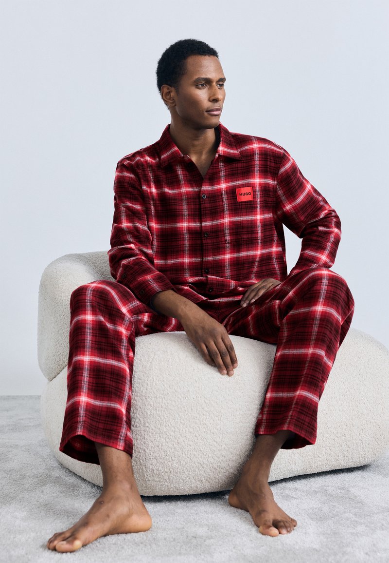 Pyjama à carreaux rouges avec une chemise boutonnée et un pantalon assorti, avec une étiquette de marque sur la poitrine. Tissu doux et coupe décontractée.