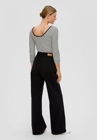 Schwarze hoch taillierte Jeans mit weitem Bein und einem hellbraunen Etikett auf der Rückseite. Kombiniert mit einem gestreiften langärmligen Oberteil mit offenem Rücken.
