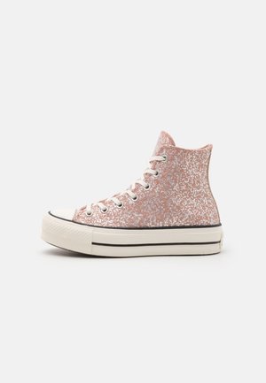 Wysokie sneakersy na platformie z różowo-białą cętkowaną tkaniną, białymi sznurowadłami i grubą białą podeszwą z czarnymi paskami, widok z boku.